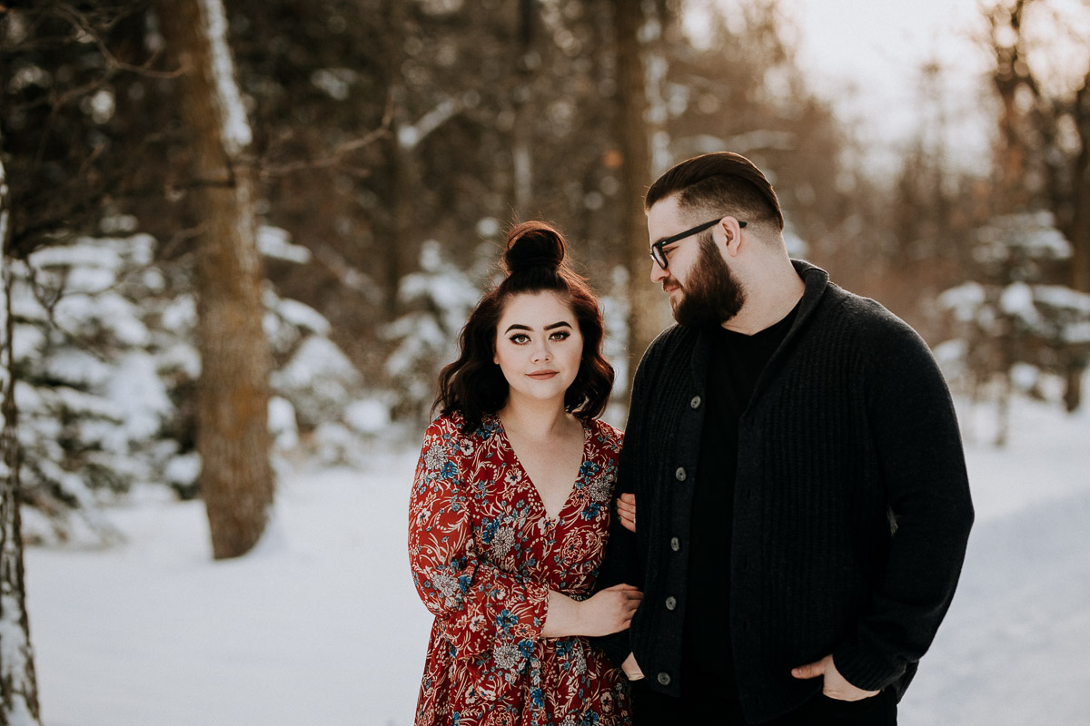 Engaged couple looking at camera at St. Vital park in winter
