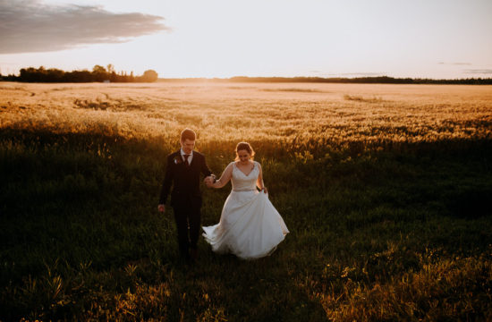 bride and groom running across field at sunset