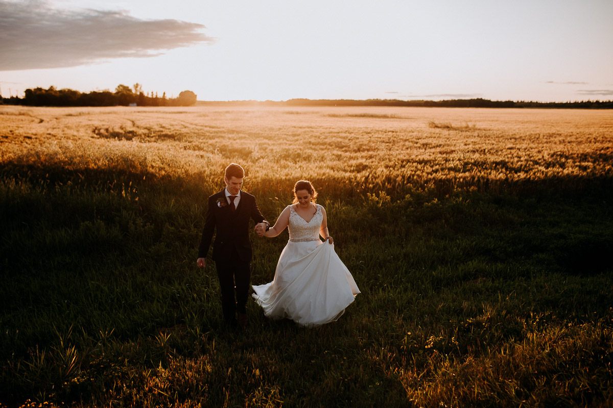 bride and groom running across field at sunset
